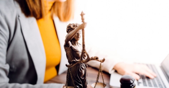 Woman lawyer on a laptop with Lady Justice statue in front of her.